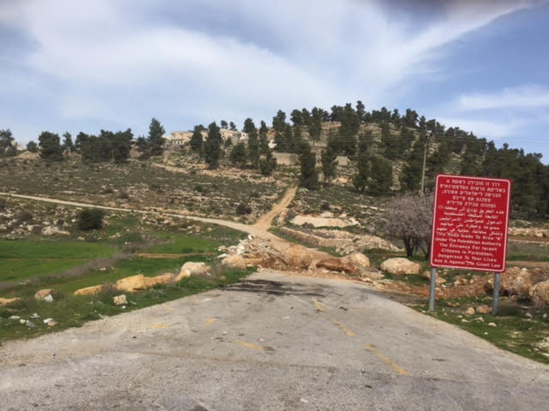 סוללה קטנה חוסמת כניסה ליישוב פלסטיני ולצידה שלט אדום המזהיר שזהו שטח A