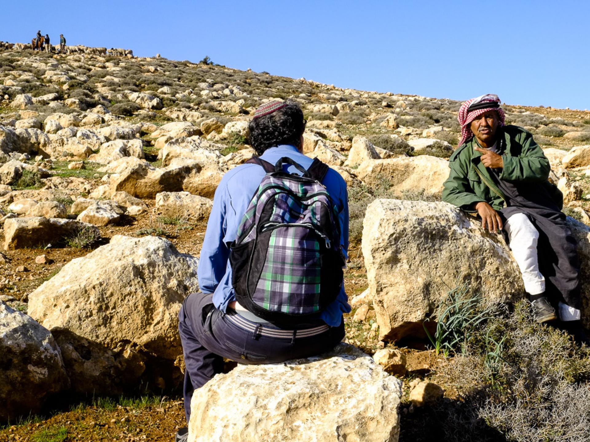 Rabbi Arik Asherman conversing with the elder shepherd – with soldiers, settlers and their flock up on the hill