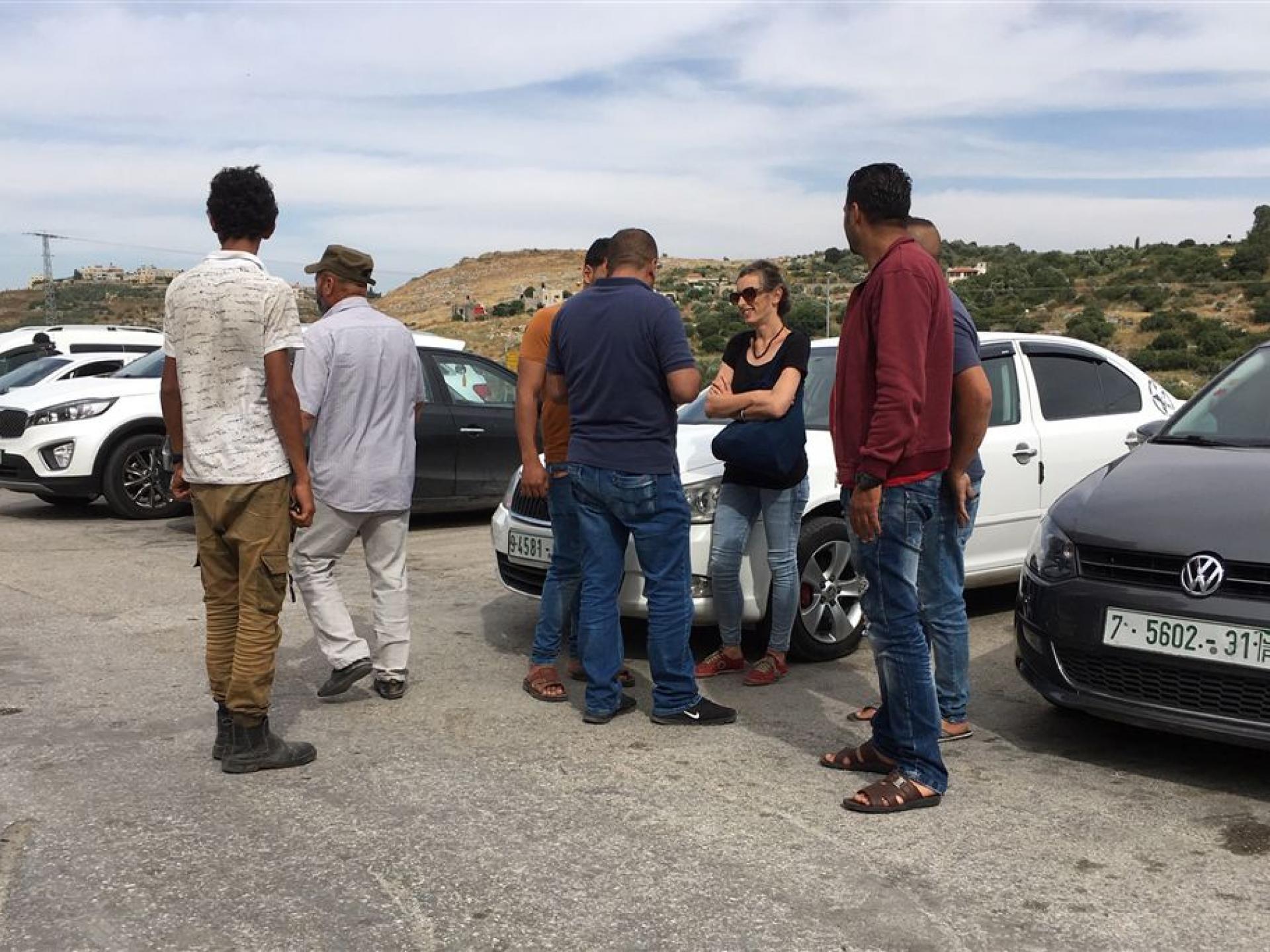 אישה באזור חניית מכוניות משוחחת עם מספר גברים