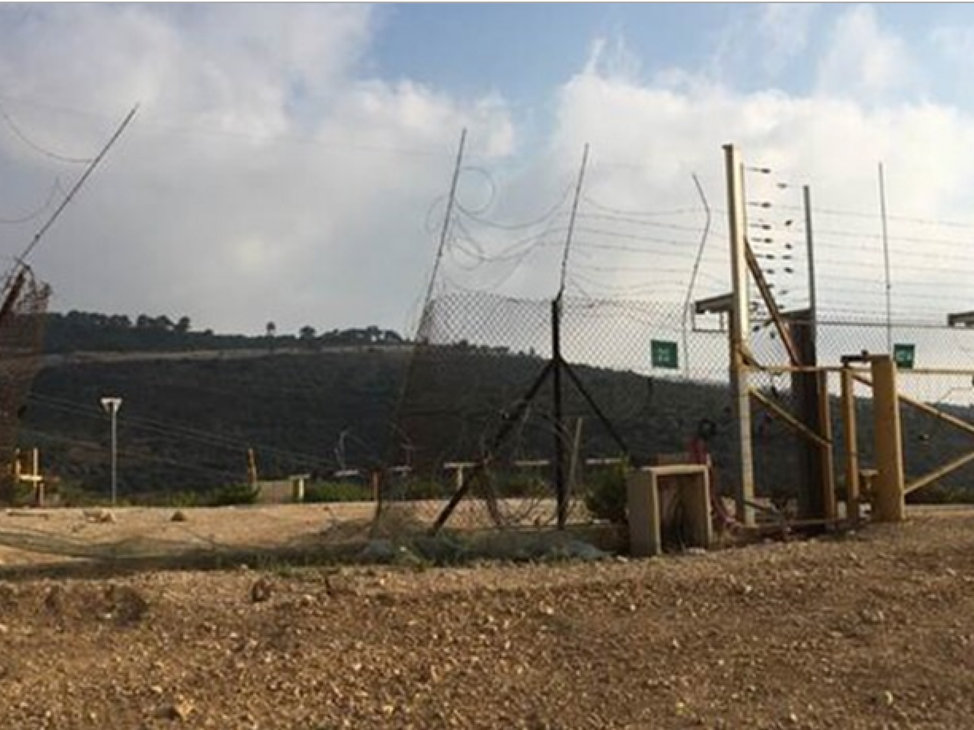 רואים שער צהוב נעול באמצע המחסום ולידו פִרצה גדולה בגדר