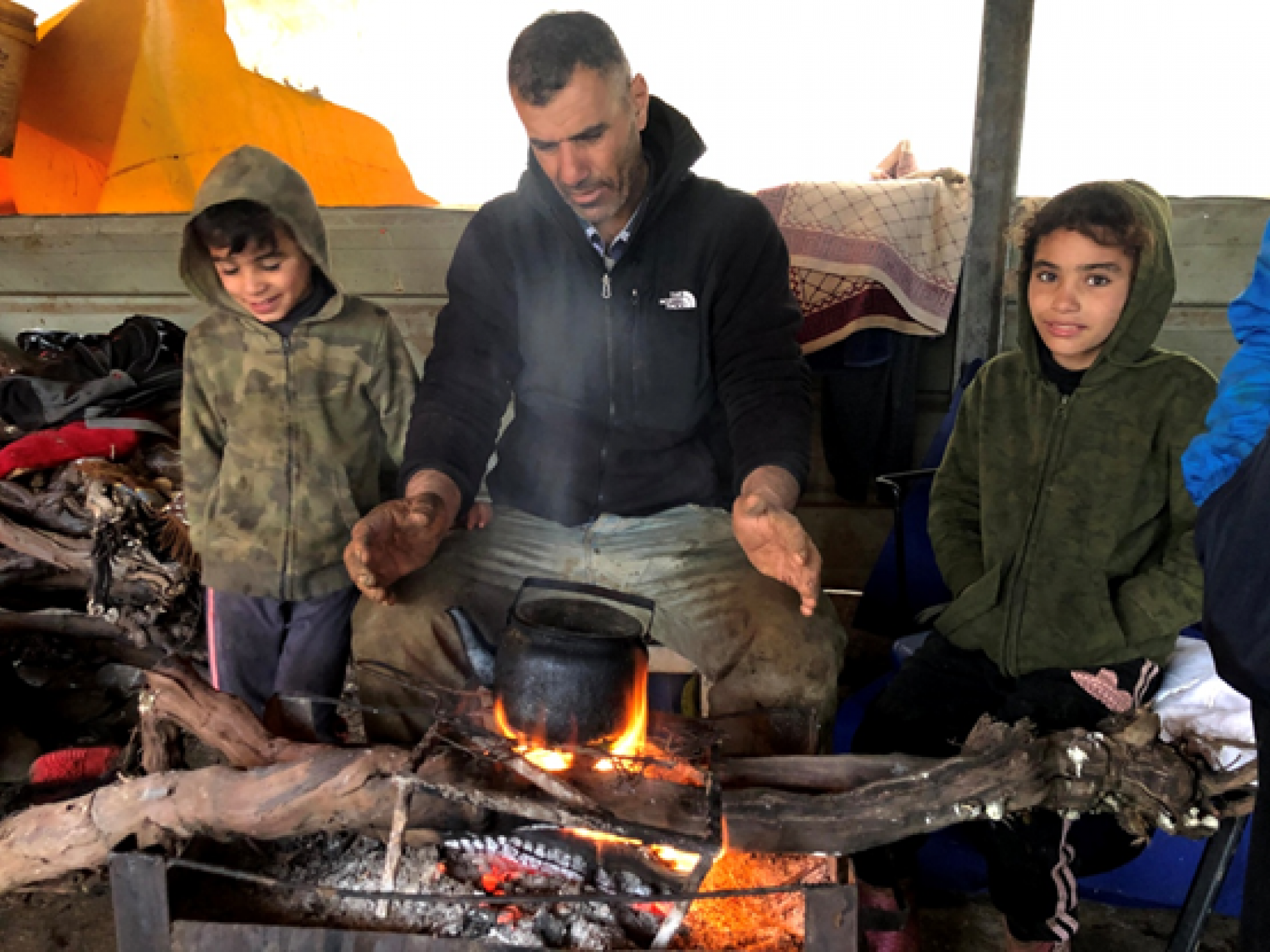 אב וילדיו מתחממים בתוך האוהל ליד תנור של גחלים בוערות