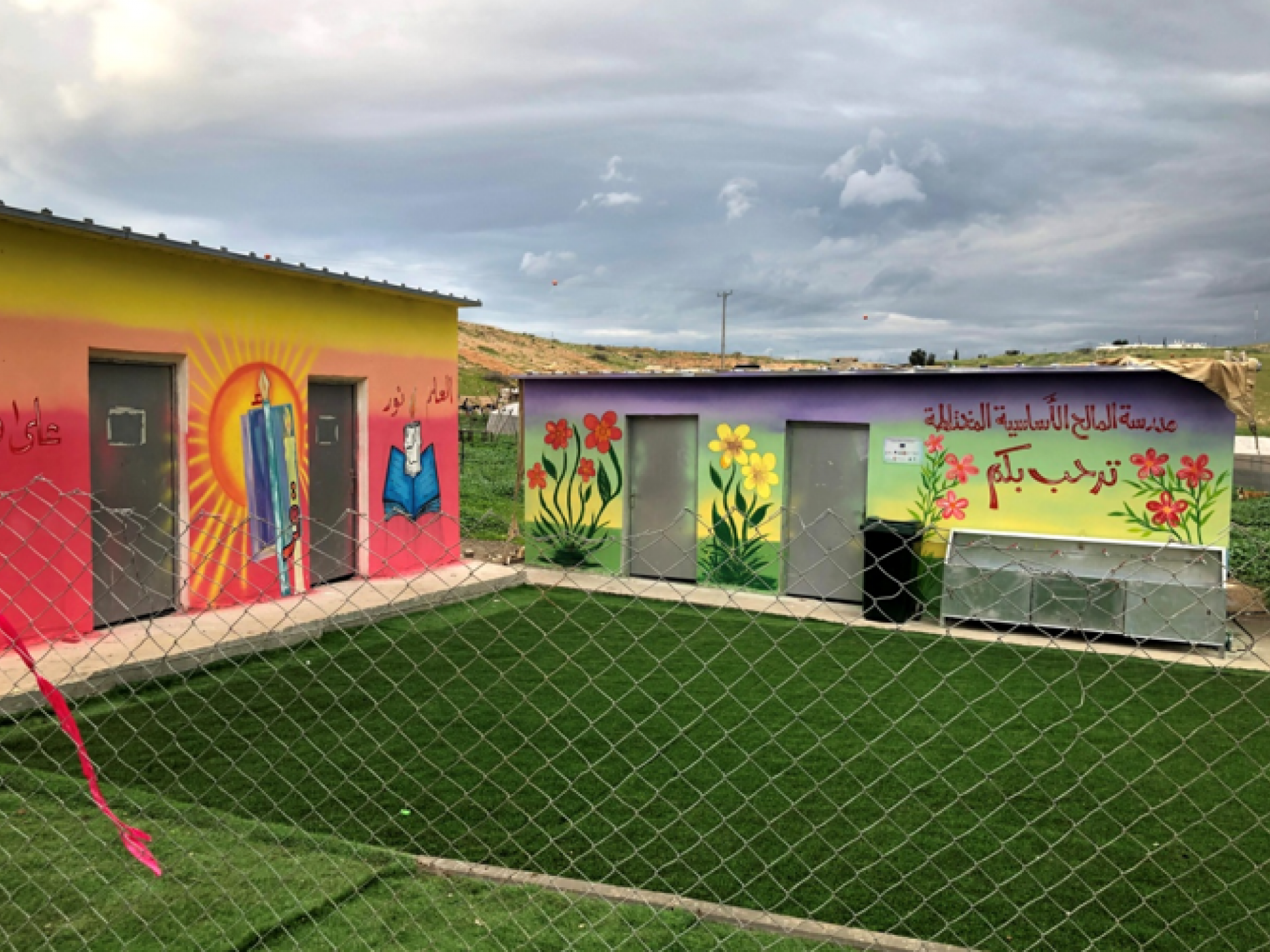 שני מבנים קטנים של בית ספר, דשא מפלסטיק ירוק מאוד וציורי קיר יפים