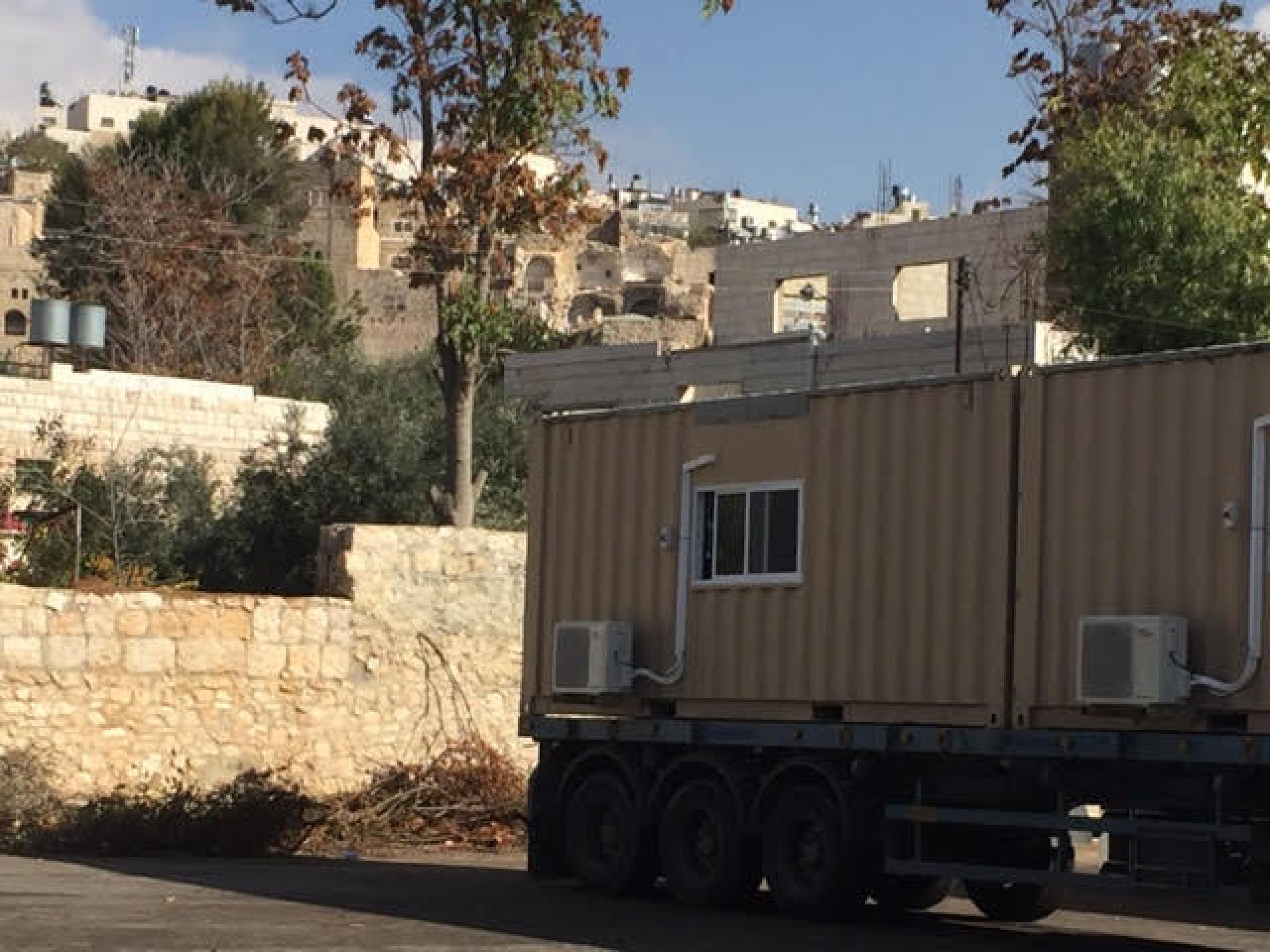 A military vehicle is driving with three mobile buildings