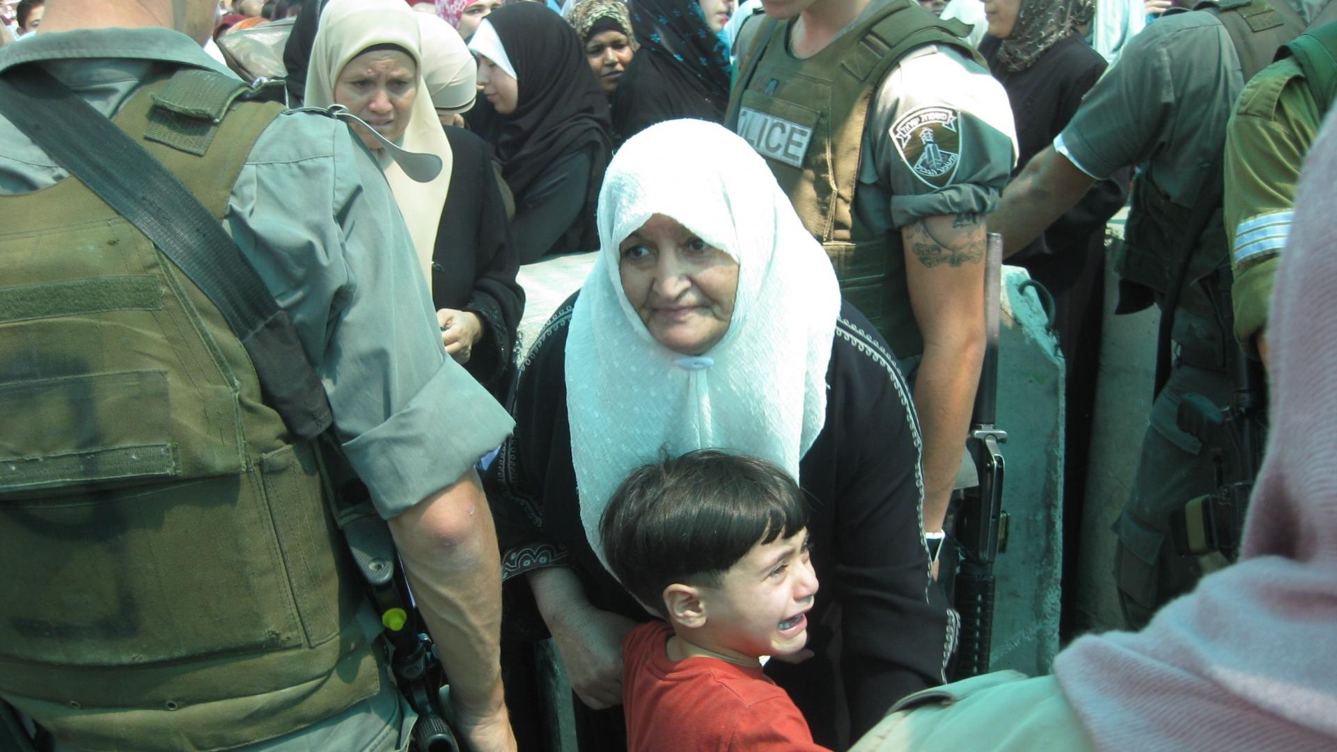 An older woman; a child crying; a soldier at the checkpoint