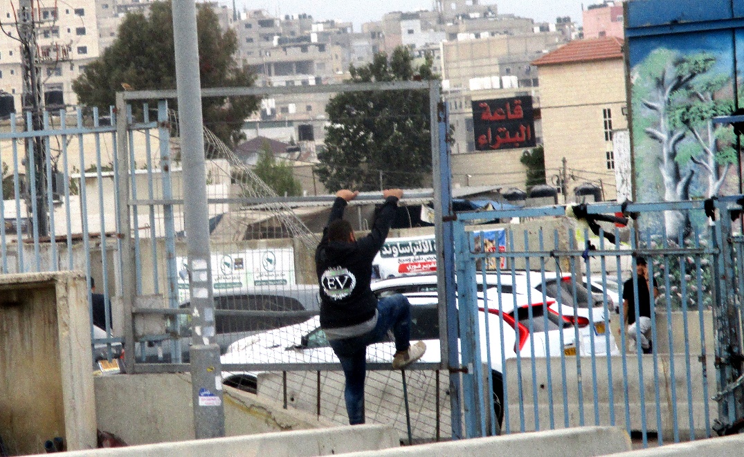 Qalandiya. Closure – Climbing over the fence